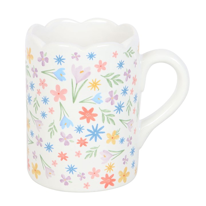 A white ceramic mug decorated with a colorful array of pastel flowers and green leaves. The mug features a unique scalloped rim and curved handle, creating a soft and cheerful springtime aesthetic.
