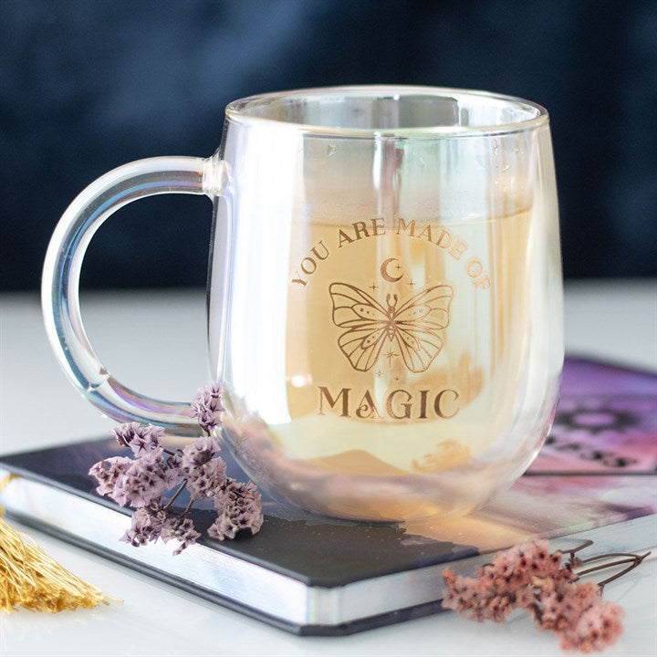 A clear double-walled glass mug with an iridescent interior, featuring a gold butterfly design and the phrase "You are made of magic" in gold lettering. The mug has a smooth handle and a modern, rounded shape.