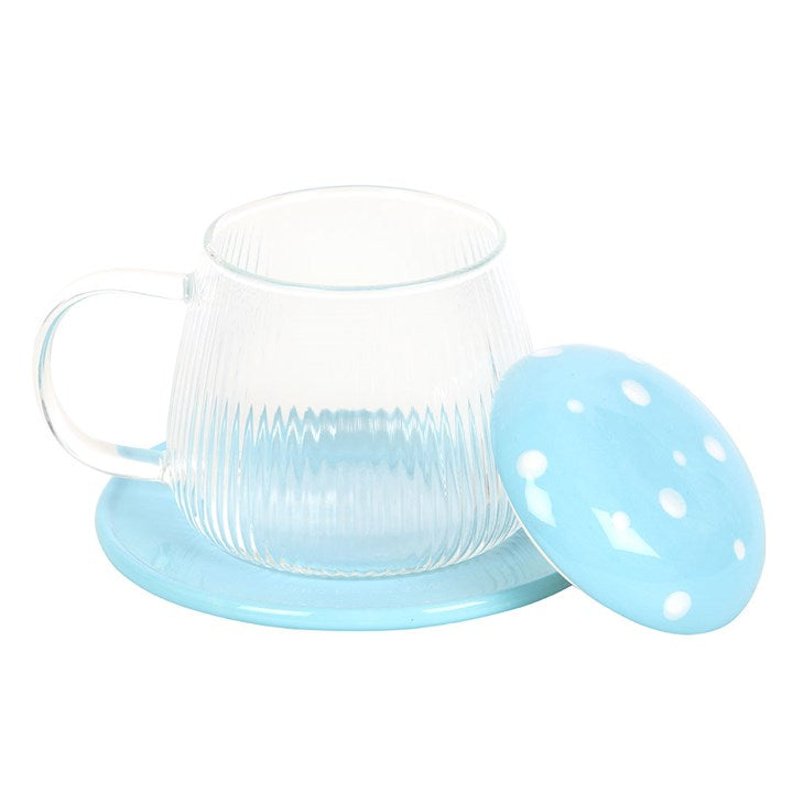 A whimsical glass mug with vertical ribbing, topped with a blue mushroom cap-style lid featuring white polka dots. The mug comes with a matching blue coaster and has a clear handle, creating a fun and cheerful aesthetic perfect for tea or coffee.