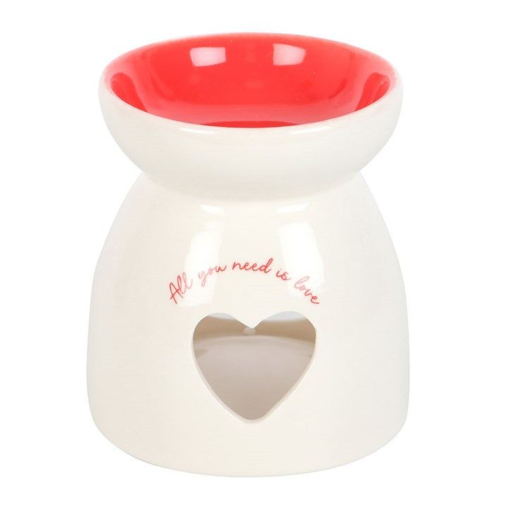 Ceramic wax melt burner with 'All You Need Is Love' text, featuring a heart-shaped cutout glowing with a tealight candle and a red interior bowl. Perfect for home fragrance lovers to create a cozy and romantic ambiance