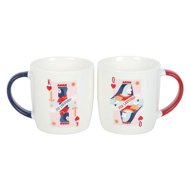 A pair of white ceramic mugs featuring playing card-inspired designs labeled “His Lordship” and “Her Ladyship.” One has a navy handle with a king of hearts motif, while the other has a red handle with a queen of hearts design. The mugs are displayed on a round white tray against a cozy navy background.