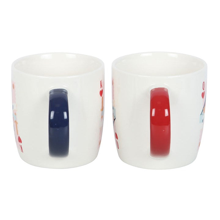 A pair of white ceramic mugs featuring playing card-inspired designs labeled “His Lordship” and “Her Ladyship.” One has a navy handle with a king of hearts motif, while the other has a red handle with a queen of hearts design. The mugs are displayed on a round white tray against a cozy navy background.