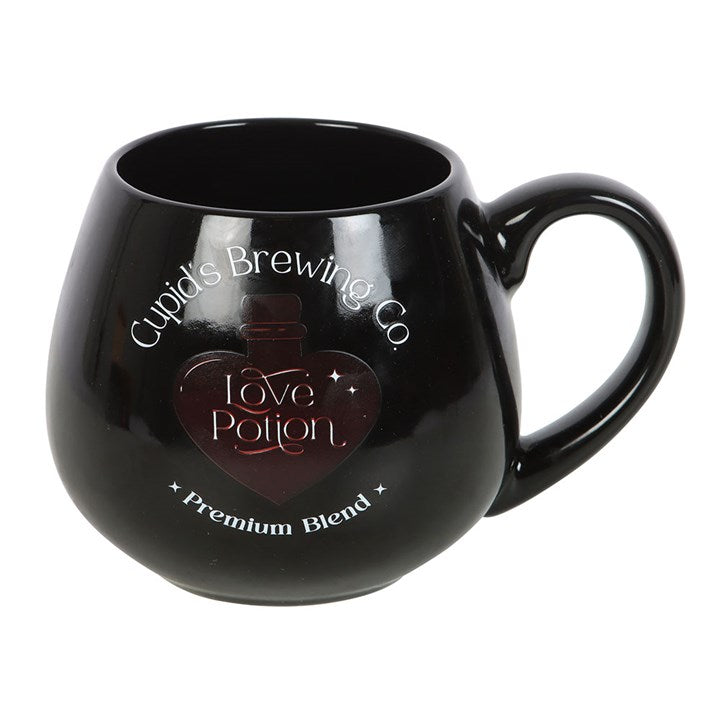 Black ceramic Love Potion heat change mug featuring 'Cupid's Brewing Co.' design with a heart-shaped potion bottle graphic that changes color when filled with a hot beverage.