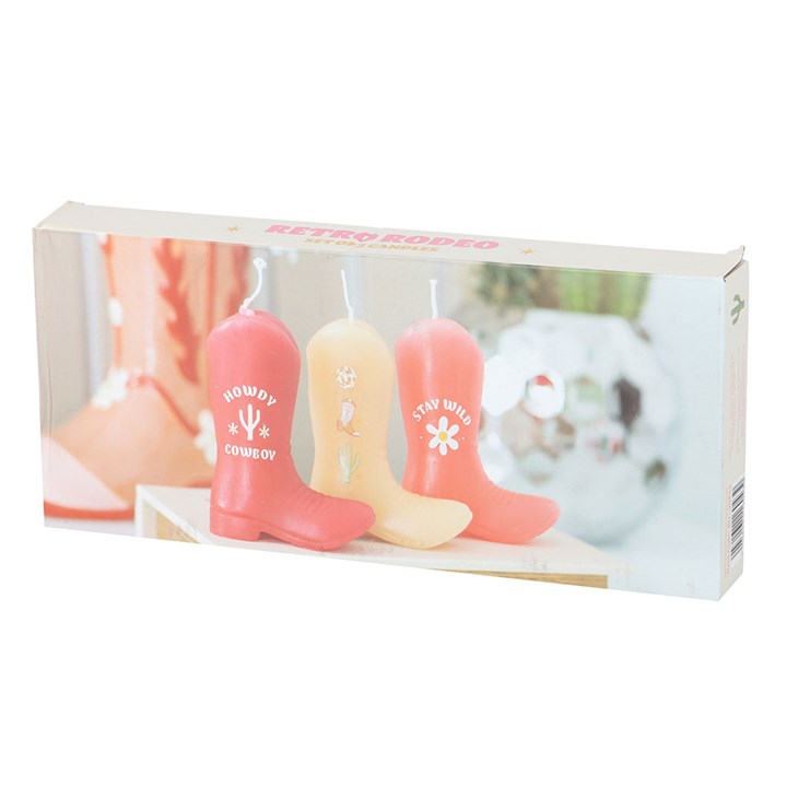 A set of three unscented decorative candles shaped like cowboy boots in shades of pink and peach. Each boot features Western-themed designs and phrases like "Howdy Cowboy" and "Stay Wild." Displayed on a wooden surface with soft background decor, adding a playful country charm.