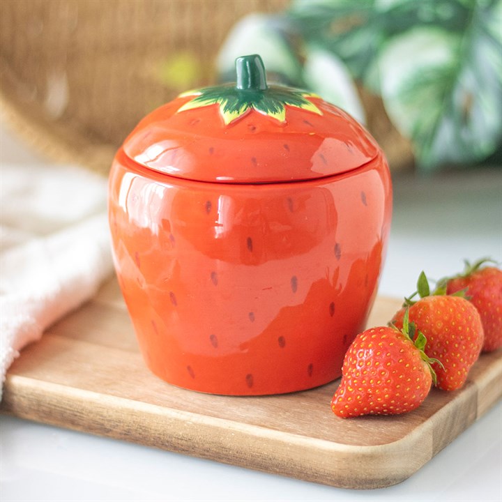 A beautifully designed strawberry-shaped scented candle housed in a glossy ceramic jar with a removable lid featuring a green leafy top.