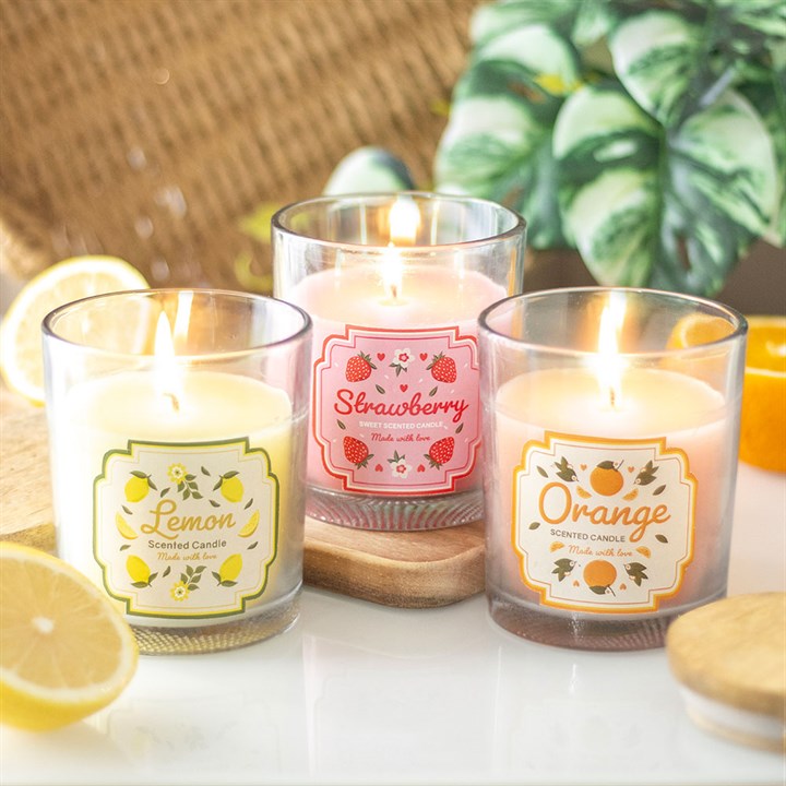 A strawberry-scented candle in a transparent glass jar with a pink floral and strawberry print label