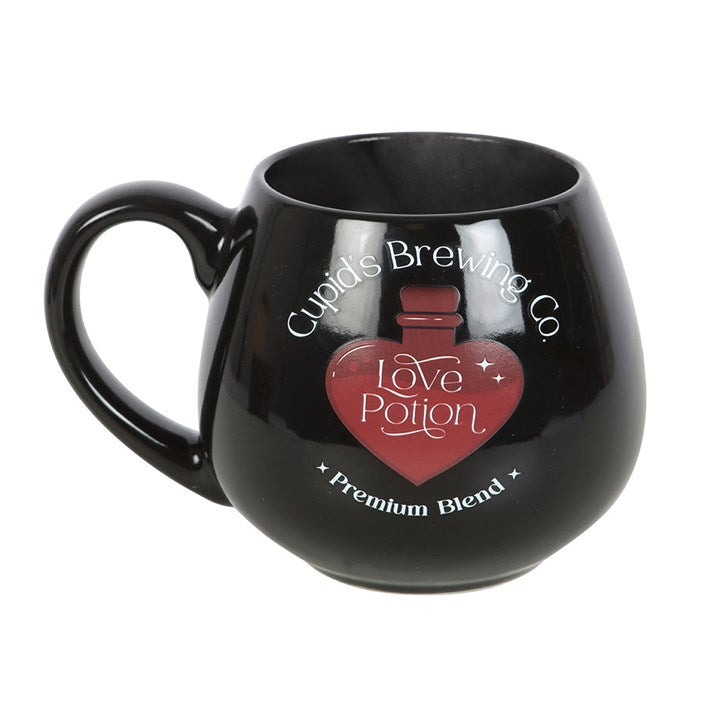 Black ceramic Love Potion heat change mug featuring 'Cupid's Brewing Co.' design with a heart-shaped potion bottle graphic that changes color when filled with a hot beverage.
