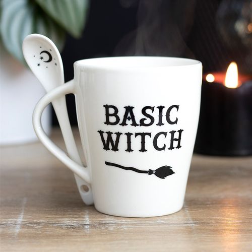 White ceramic mug with 'Basic Witch' text and a broom design, accompanied by a matching spoon featuring a crescent moon and stars. Dishwasher and microwave safe, perfect for witchy and Halloween lovers.