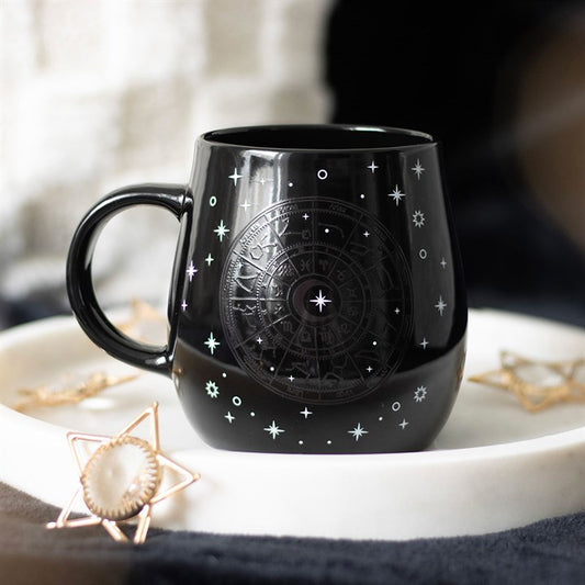 Black heat-changing celestial mug featuring a gold Astrology Wheel design surrounded by twinkling stars. The design appears when a hot beverage is poured in. 500ml capacity, dishwasher safe, not microwave safe