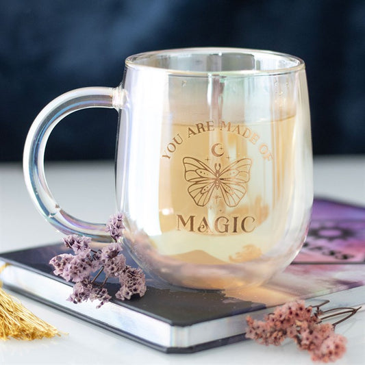 A clear double-walled glass mug with an iridescent interior, featuring a gold butterfly design and the phrase "You are made of magic" in gold lettering. The mug has a smooth handle and a modern, rounded shape.