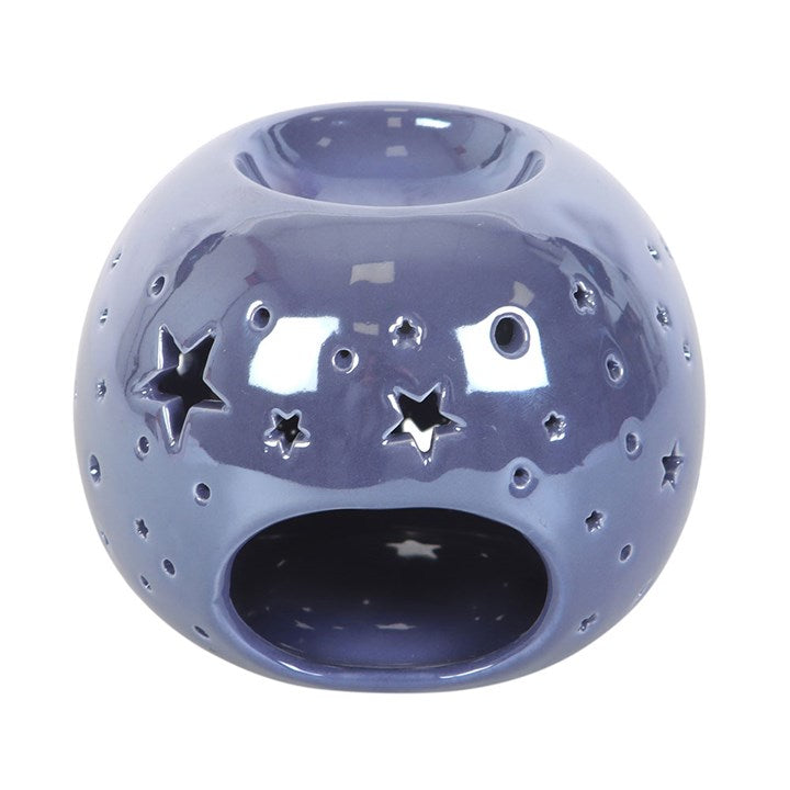 A round, purple iridescent oil burner with star and circle cut-outs that allow light to shine through. It sits beside a small essential oil bottle on a smooth surface, creating a dreamy and calming atmosphere ideal for relaxation.