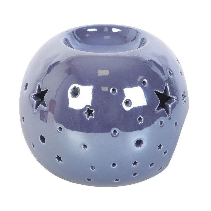 A round, purple iridescent oil burner with star and circle cut-outs that allow light to shine through. It sits beside a small essential oil bottle on a smooth surface, creating a dreamy and calming atmosphere ideal for relaxation.
