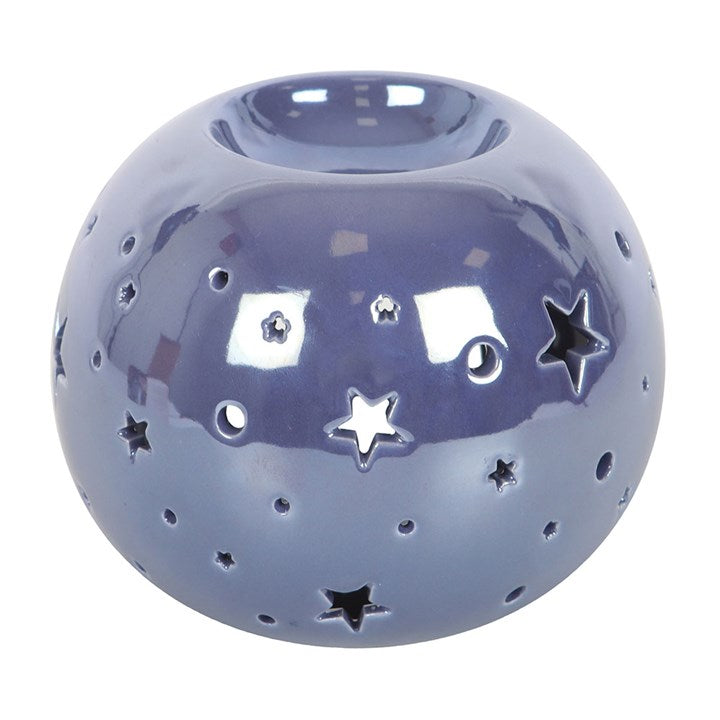 A round, purple iridescent oil burner with star and circle cut-outs that allow light to shine through. It sits beside a small essential oil bottle on a smooth surface, creating a dreamy and calming atmosphere ideal for relaxation.