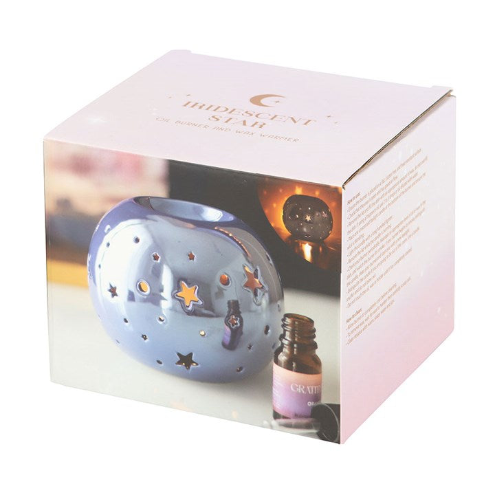 A round, purple iridescent oil burner with star and circle cut-outs that allow light to shine through. It sits beside a small essential oil bottle on a smooth surface, creating a dreamy and calming atmosphere ideal for relaxation.