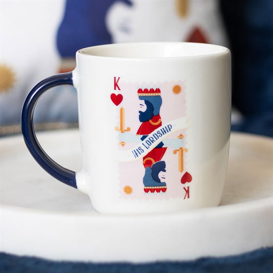 A white ceramic mug with a navy handle, featuring a king of hearts playing card illustration and the phrase “His Lordship.” The mug sits on a round white tray, offering a refined and playful design perfect for the royal gentleman in your life.
