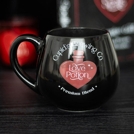 Black ceramic Love Potion heat change mug featuring 'Cupid's Brewing Co.' design with a heart-shaped potion bottle graphic that changes color when filled with a hot beverage.