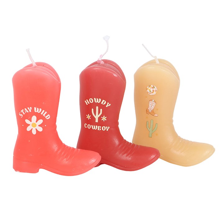 A set of three unscented decorative candles shaped like cowboy boots in shades of pink and peach. Each boot features Western-themed designs and phrases like "Howdy Cowboy" and "Stay Wild." Displayed on a wooden surface with soft background decor, adding a playful country charm.