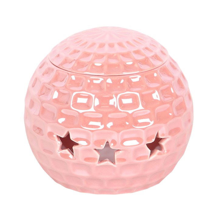 A glossy pink ceramic oil burner shaped like a disco ball, featuring star-shaped cut-outs. The burner sits atop a closed book, surrounded by soft, decorative elements, adding a fun and nostalgic touch to the space.