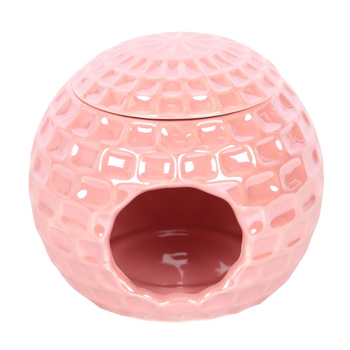 A glossy pink ceramic oil burner shaped like a disco ball, featuring star-shaped cut-outs. The burner sits atop a closed book, surrounded by soft, decorative elements, adding a fun and nostalgic touch to the space.