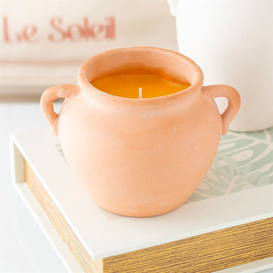 A rustic terracotta pot candle with artisan-style handles, filled with yellow citronella wax. Displayed on stacked books and decorative paper, the candle adds both natural charm and practical insect-repelling function to outdoor or indoor spaces.