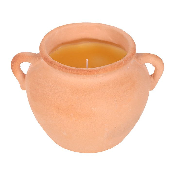 A rustic terracotta pot candle with artisan-style handles, filled with yellow citronella wax. Displayed on stacked books and decorative paper, the candle adds both natural charm and practical insect-repelling function to outdoor or indoor spaces.