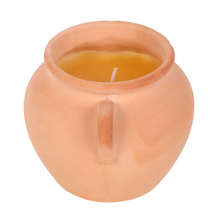 A rustic terracotta pot candle with artisan-style handles, filled with yellow citronella wax. Displayed on stacked books and decorative paper, the candle adds both natural charm and practical insect-repelling function to outdoor or indoor spaces.
