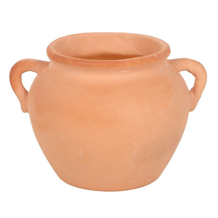 A rustic terracotta pot candle with artisan-style handles, filled with yellow citronella wax. Displayed on stacked books and decorative paper, the candle adds both natural charm and practical insect-repelling function to outdoor or indoor spaces.