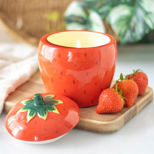 A beautifully designed strawberry-shaped scented candle housed in a glossy ceramic jar with a removable lid featuring a green leafy top.