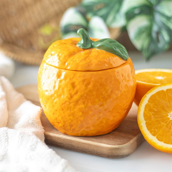 A beautifully designed orange-shaped scented candle housed in a glossy ceramic jar with a removable lid, featuring a green leaf accent. 