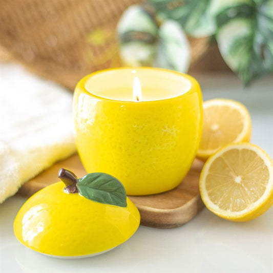 A lemon-shaped scented candle in a glossy ceramic jar with a removable lid, featuring a green leaf accent. 
