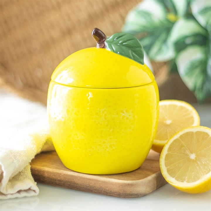 A lemon-shaped scented candle in a glossy ceramic jar with a removable lid, featuring a green leaf accent. 