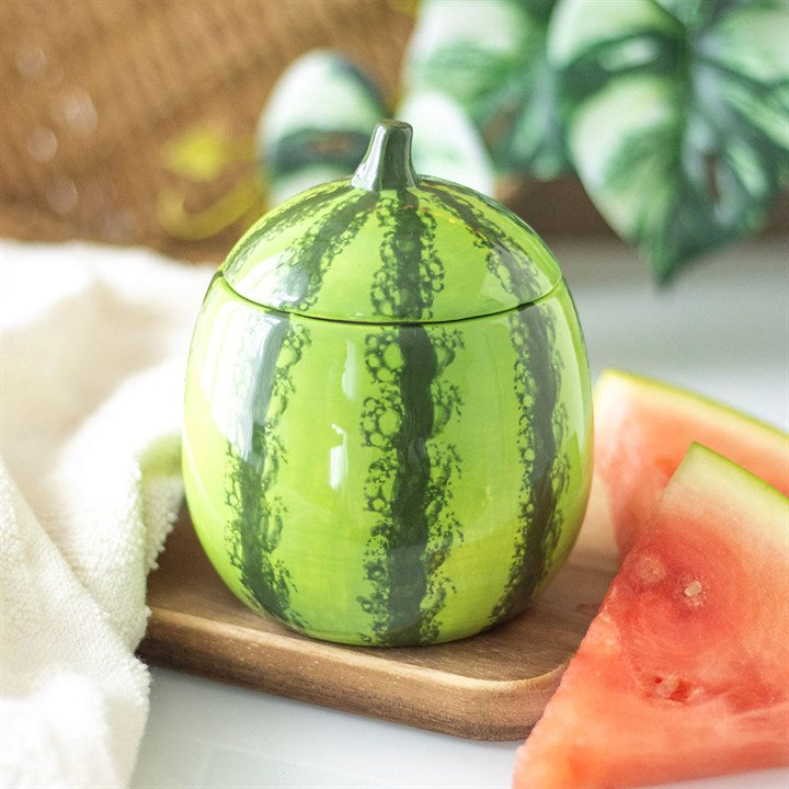 A watermelon-shaped scented candle in a glossy ceramic jar with a removable lid, featuring a realistic green rind design.