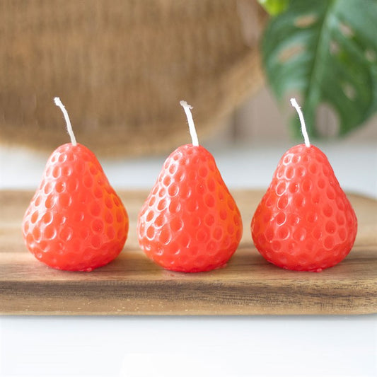 A set of three unscented, strawberry-shaped candles with a textured surface, placed on a wooden board. The candles have a vibrant red-orange hue and white wicks, adding a decorative touch