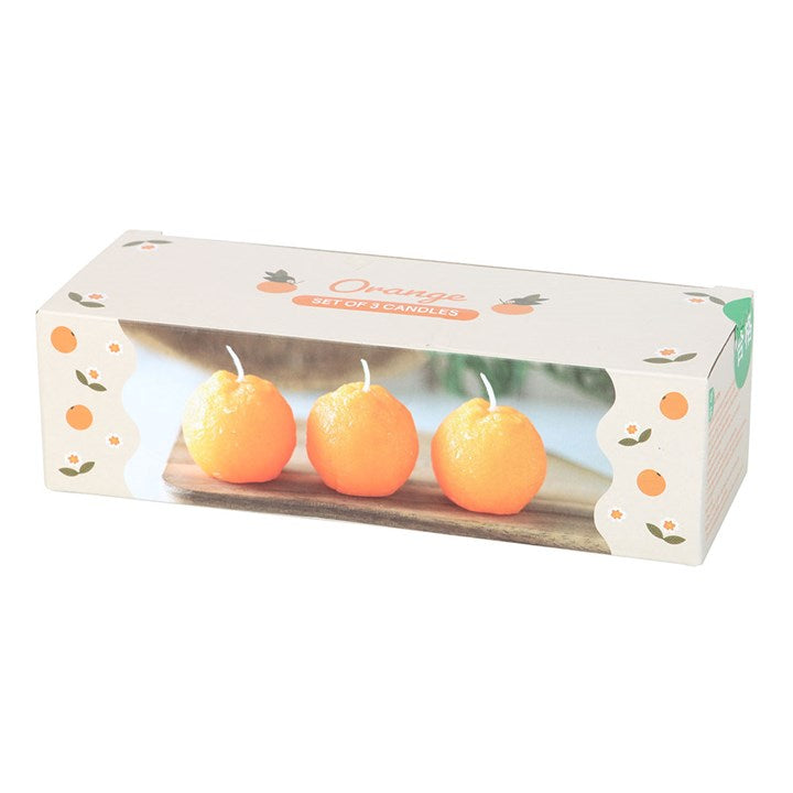 A set of three unscented, orange-shaped candles with a textured surface, placed on a wooden board. The candles have a bright orange hue and white wicks, resembling real oranges. 