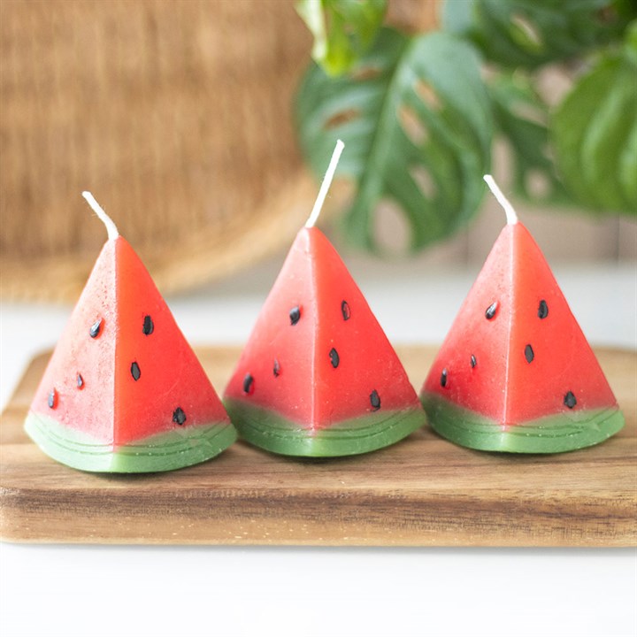 A set of three unscented, watermelon-shaped candles with a triangular design, featuring a red wax body with black seed-like details and a green base
