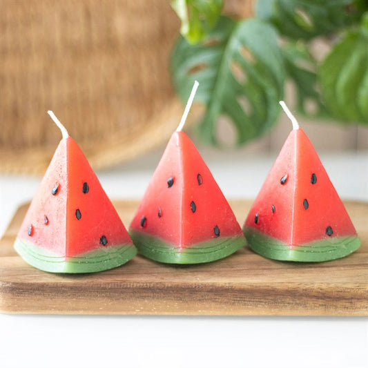 A set of three unscented, watermelon-shaped candles with a triangular design, featuring a red wax body with black seed-like details and a green base