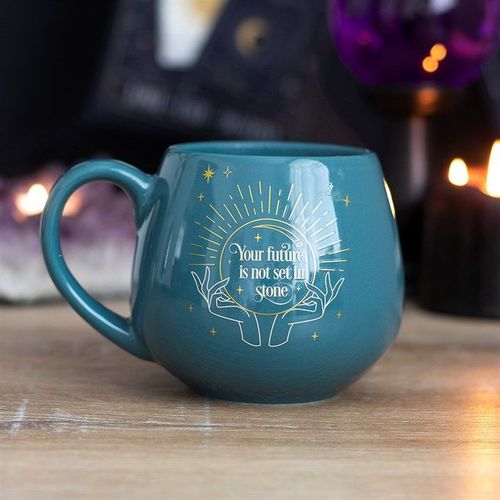 A dark green ceramic mug with a rounded shape and a gold mystical crystal ball design. The phrase “Your future is not set in stone” appears within the crystal ball. The mug features a color-change element that reveals the hidden message when filled with a hot drink.
